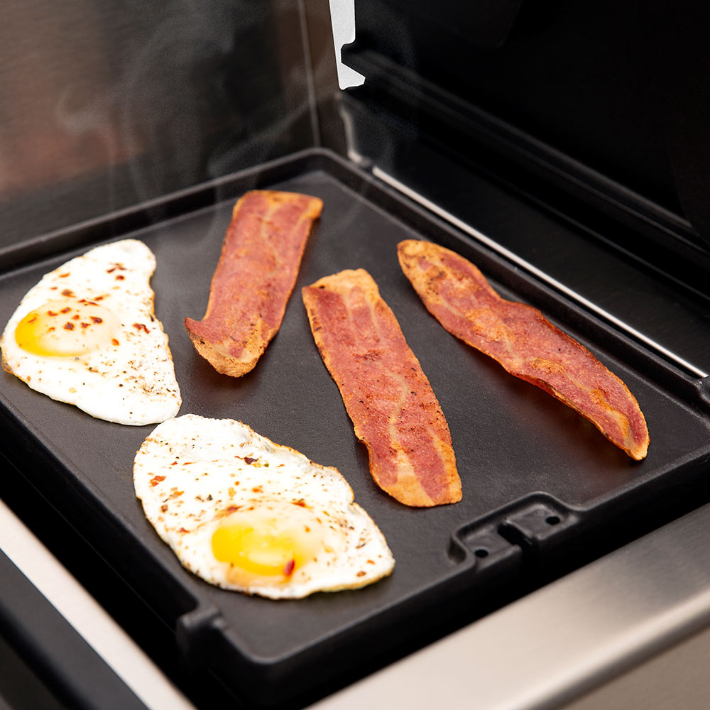 Cast iron griddle insert with sunny-side eggs and bacon strips on black plate