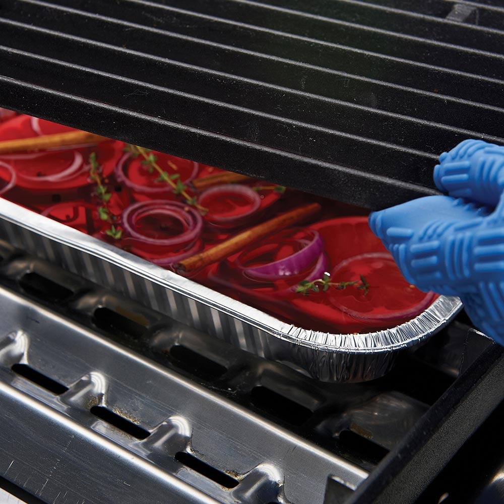 Foil narrow drip pan in grill with red food, blue tool lifting the rim