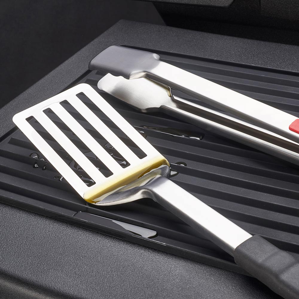 Silicone grill side shelf mat with ridged grooves, grill utensils resting on it