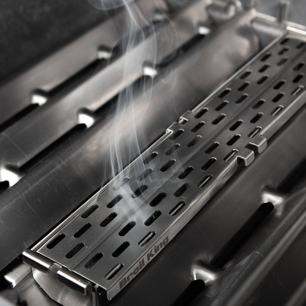 Perforated stainless steel smoker tray with smoke rising above the grilling grate