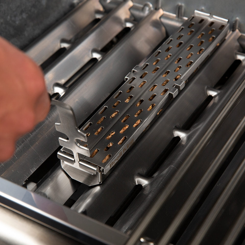Perforated stainless steel smoker tray holding brown pellets, close-up on the grate
