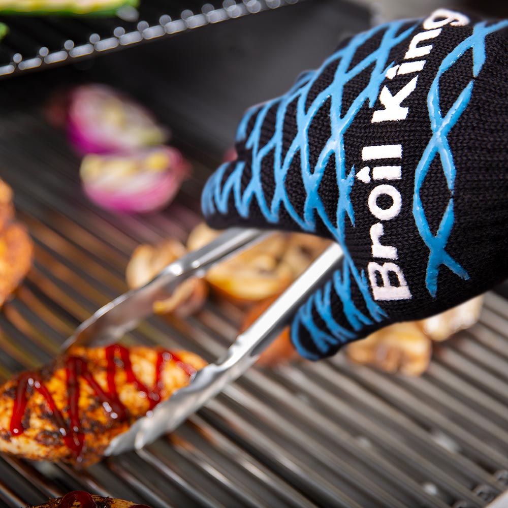 Broil King grilling mitt with blue print, holding tongs over grill