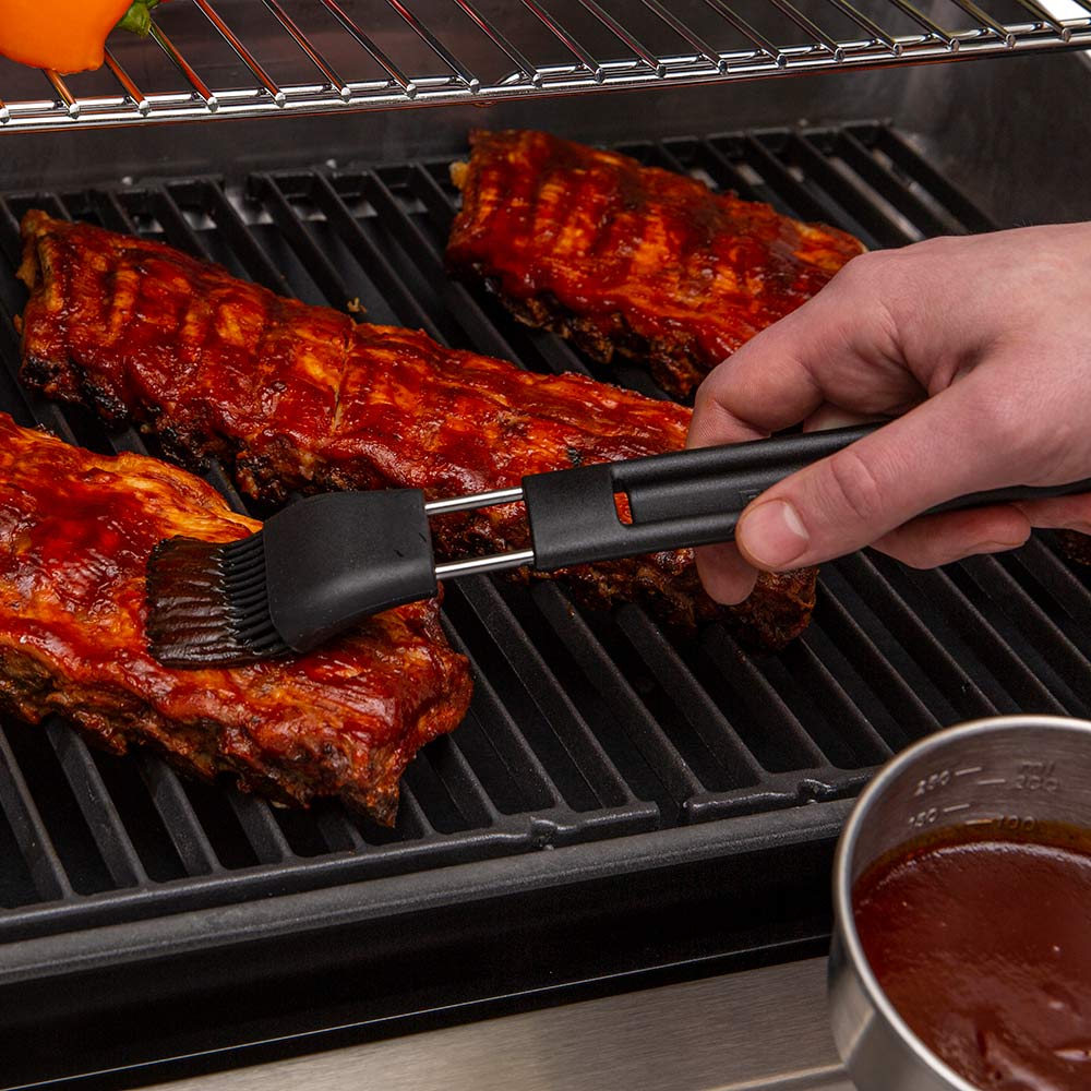 Black basting brush applying sauce to grilled meat with sauce cup