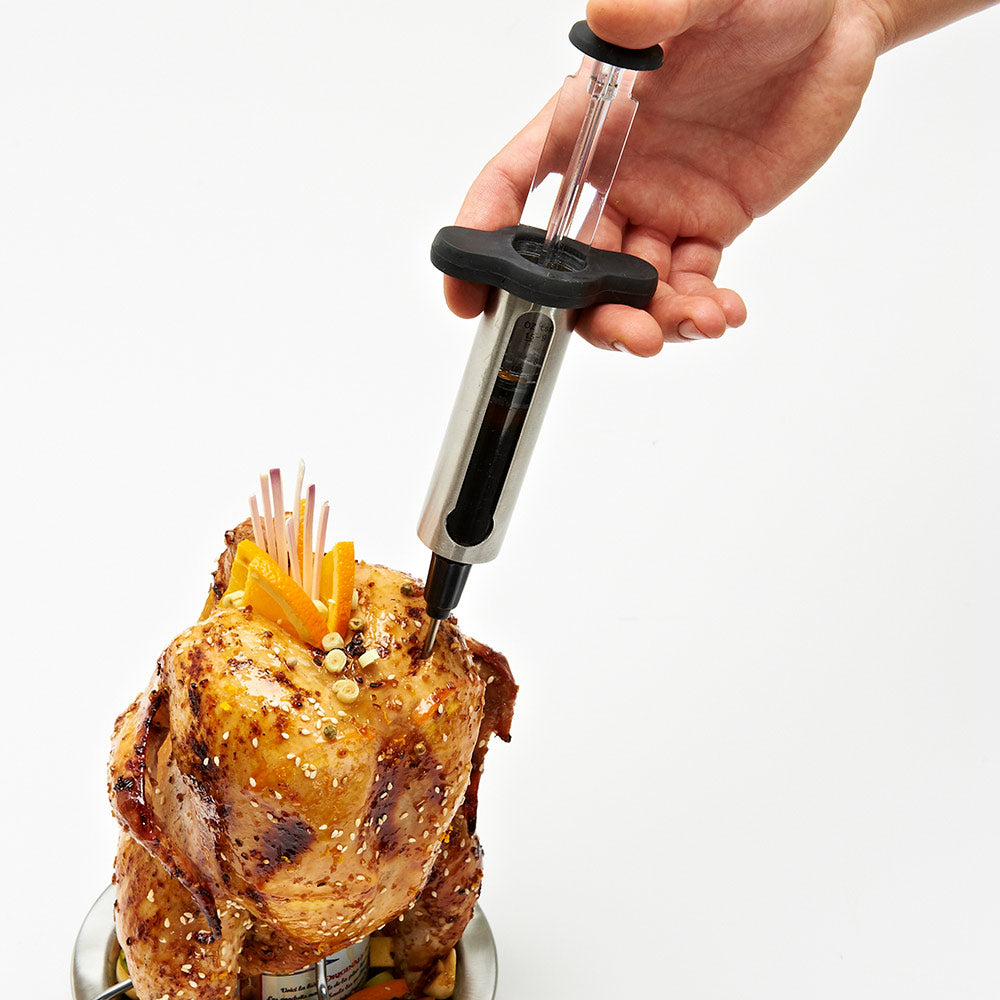 Hand holding marinade injector pressing into roast chicken on a plate