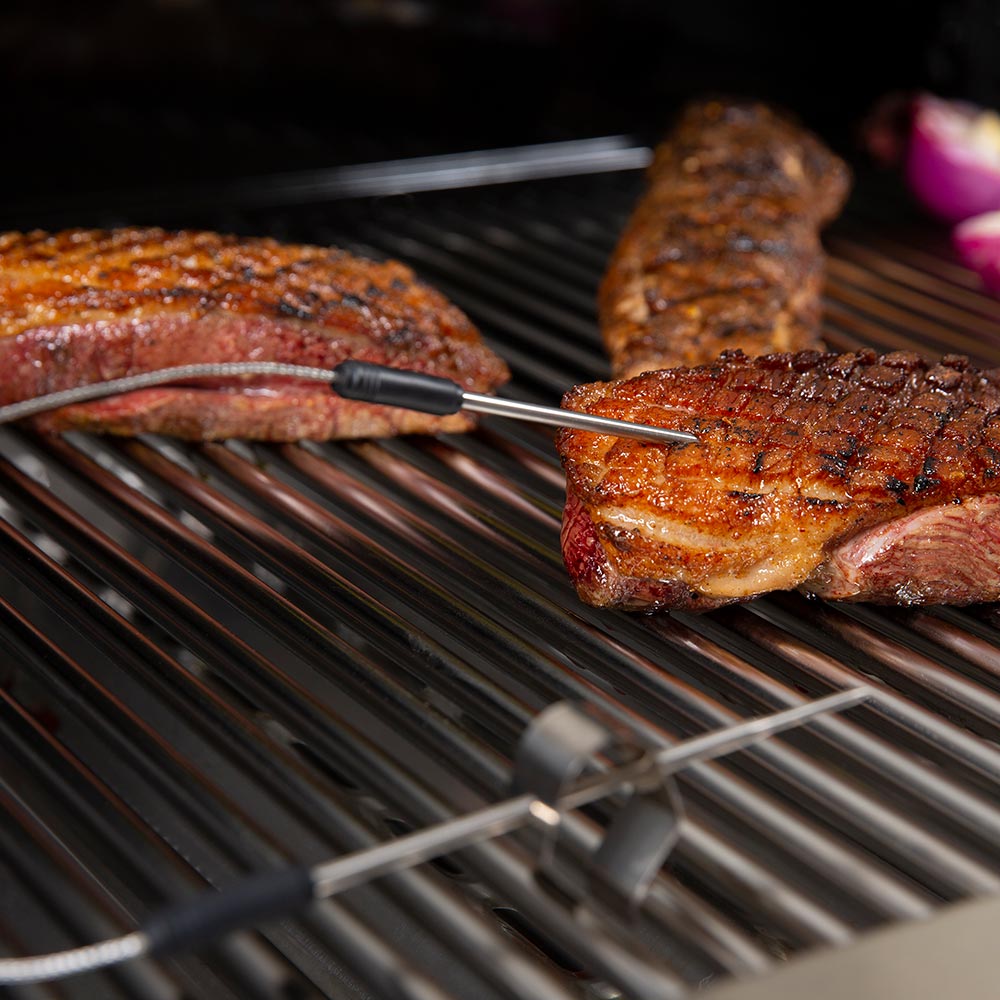 Stainless temperature probe inserted into grilled meat on metal grill grates
