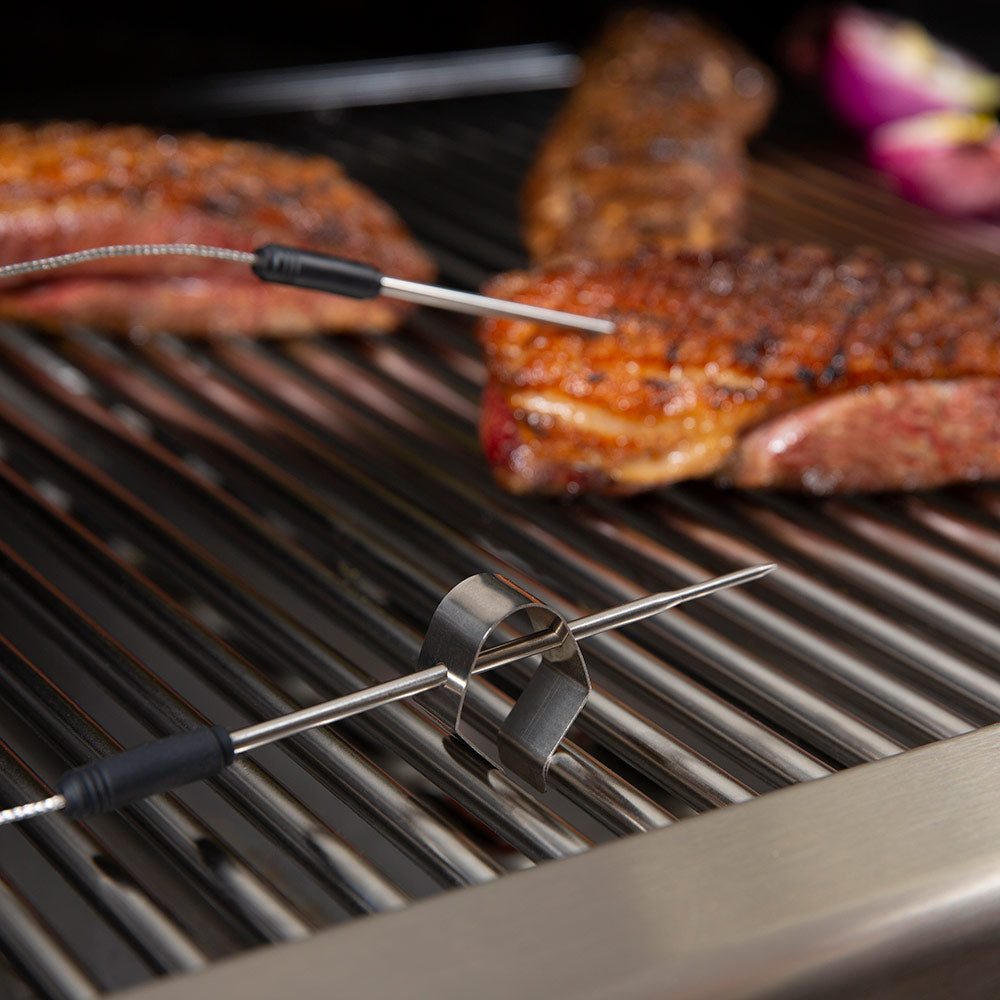 Stainless probe and thermometer wires on grill grates with grilled meat in view