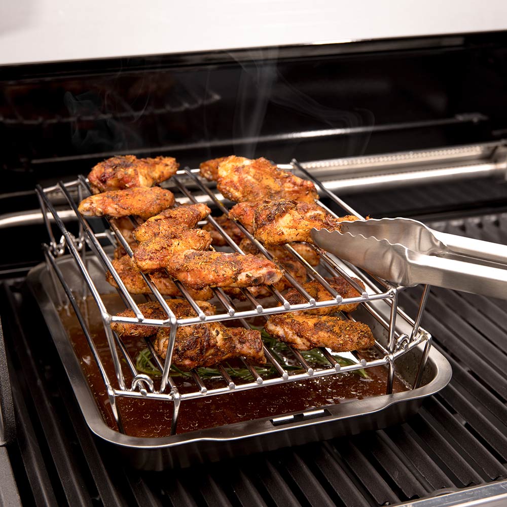 Stainless steel rack with assorted meat pieces on grill grates, smoke rising