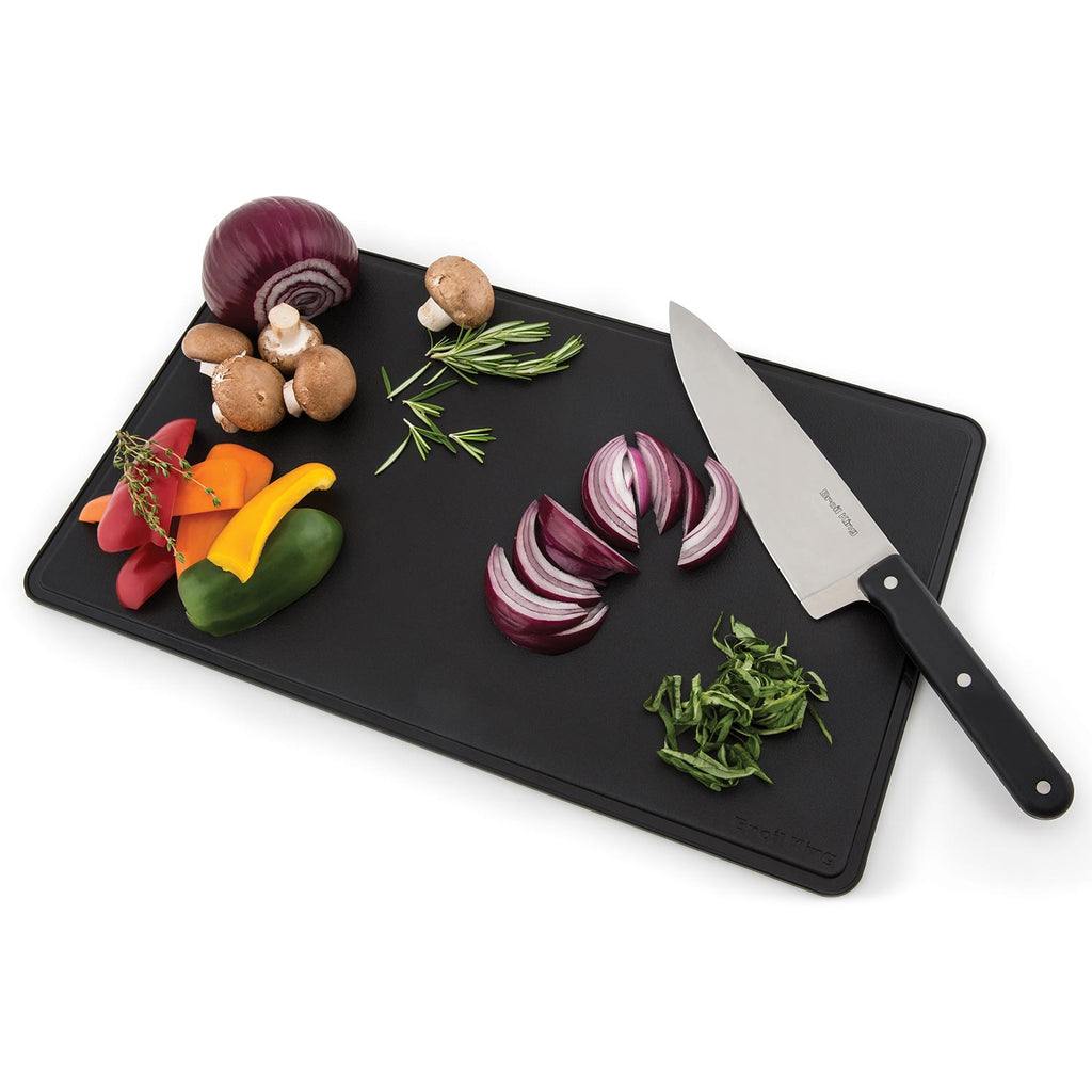Black cutting board with chef knife and assorted vegetables for grilling prep