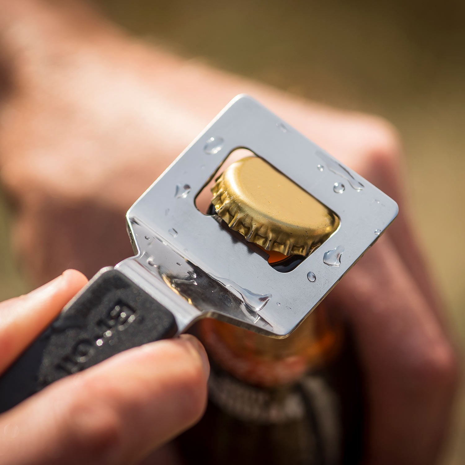 Stainless steel bottle opener pressing a bottle cap; gold cap seated in opening