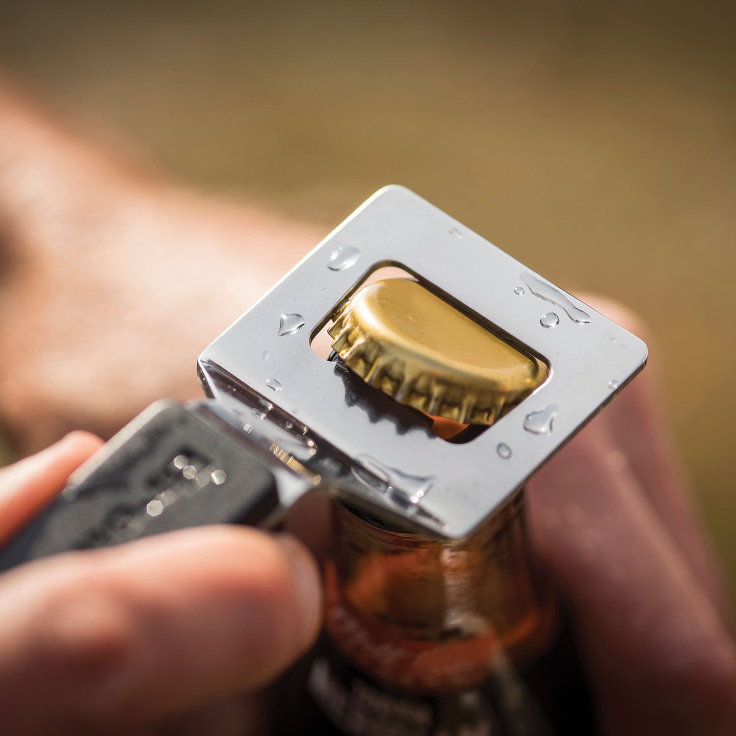 Stainless steel bottle opener held by hand, gold bottle cap in the metal slot