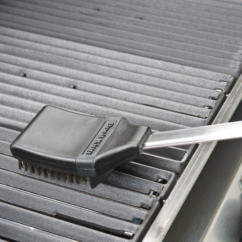 Grill brush on metal grill grates with gray bristles and black base.