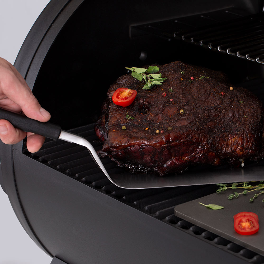 Grill flipper spatula with stainless blade and black handle lifting food from grill