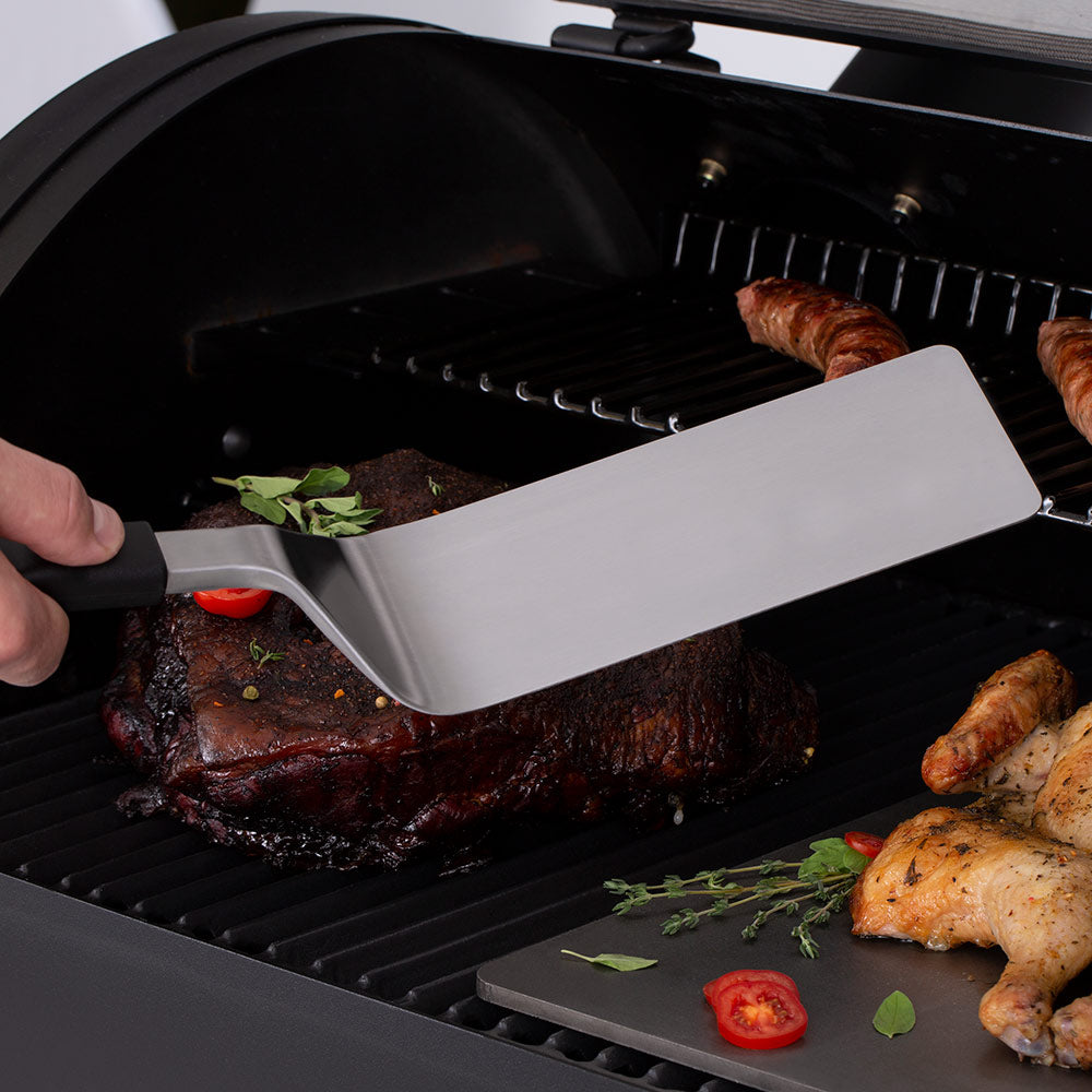 Grill flipper spatula with wide stainless blade and black handle in open grill