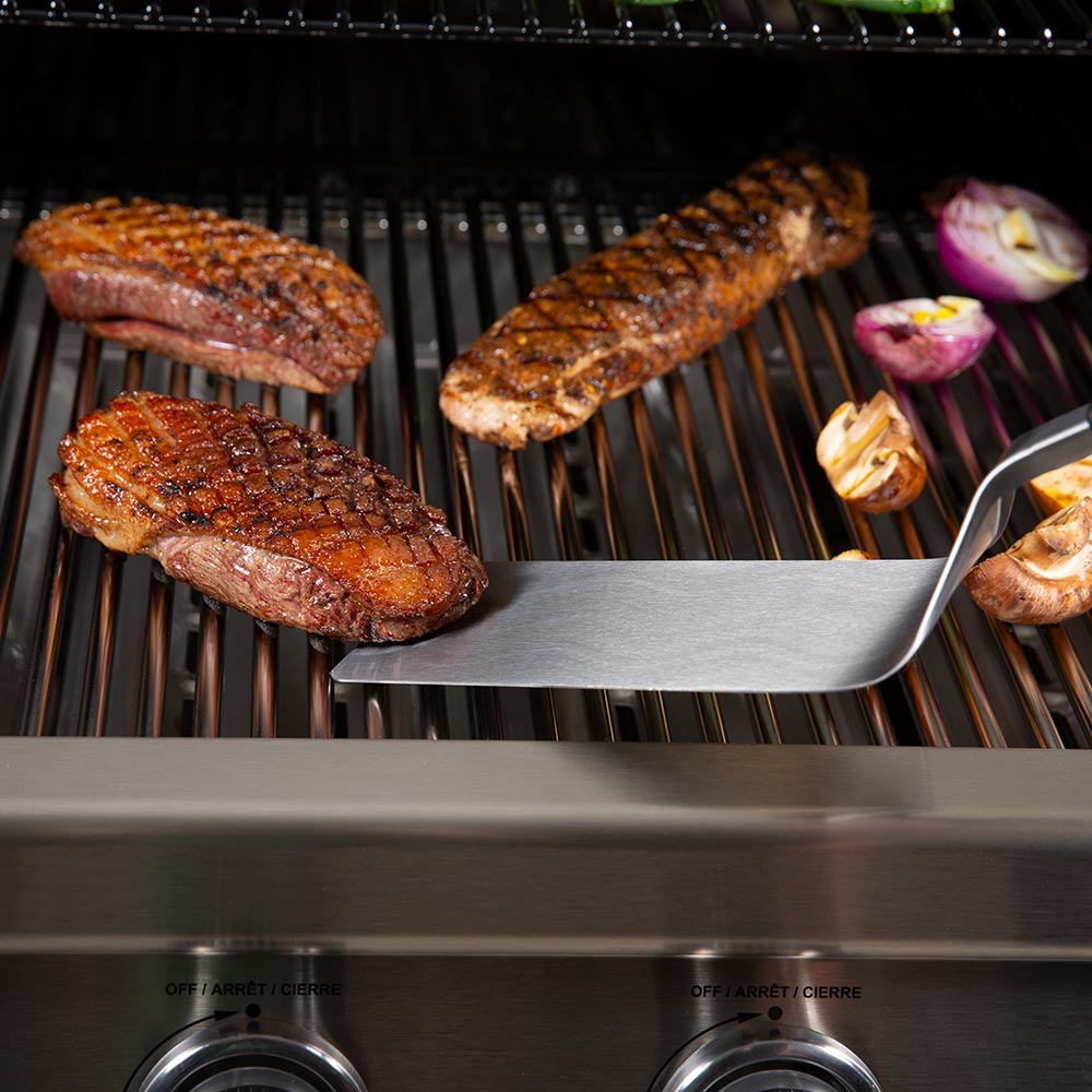 Stainless steel spatula flipper resting on grill grates with black handle