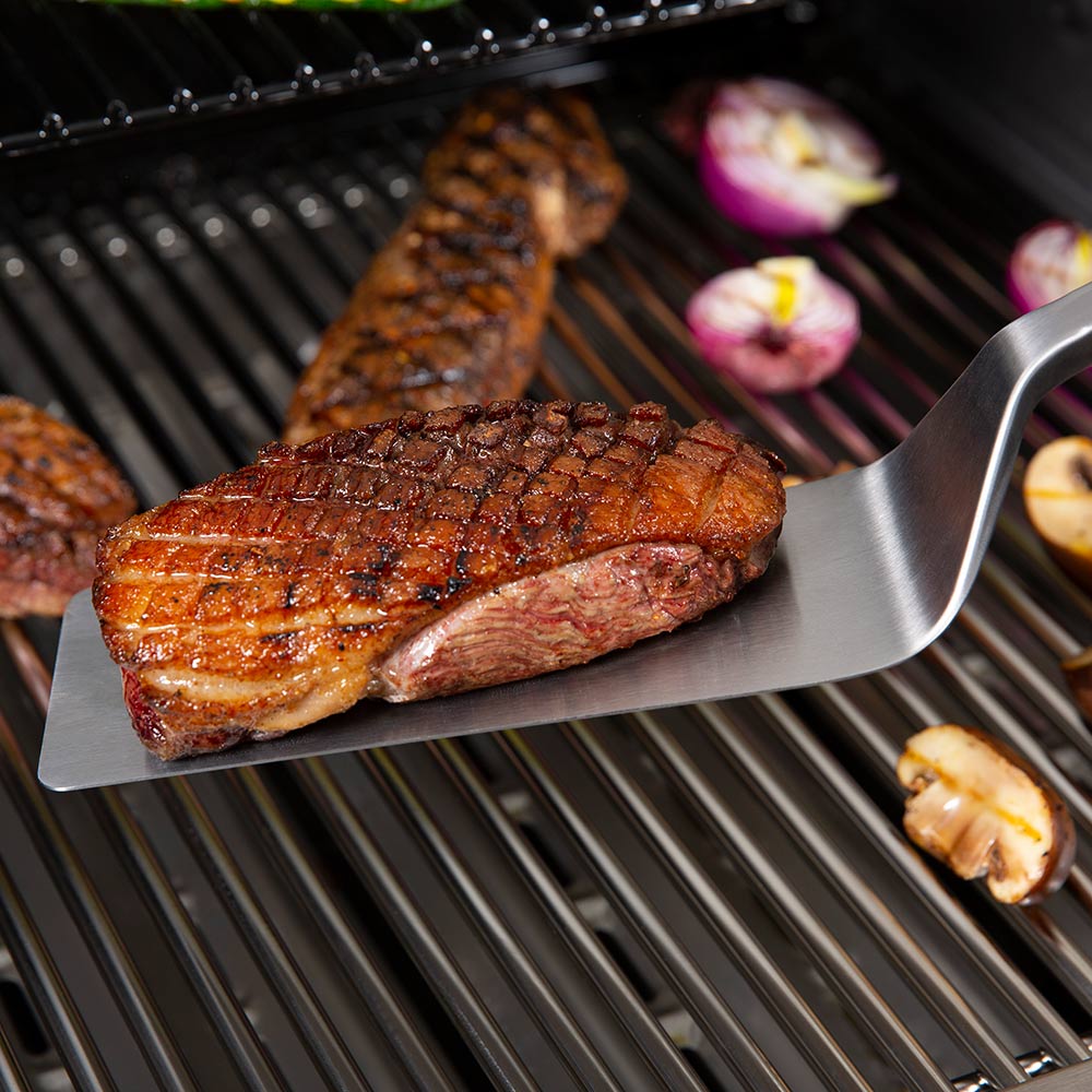 Stainless grill flipper spatula with black handle serving a grilled cut