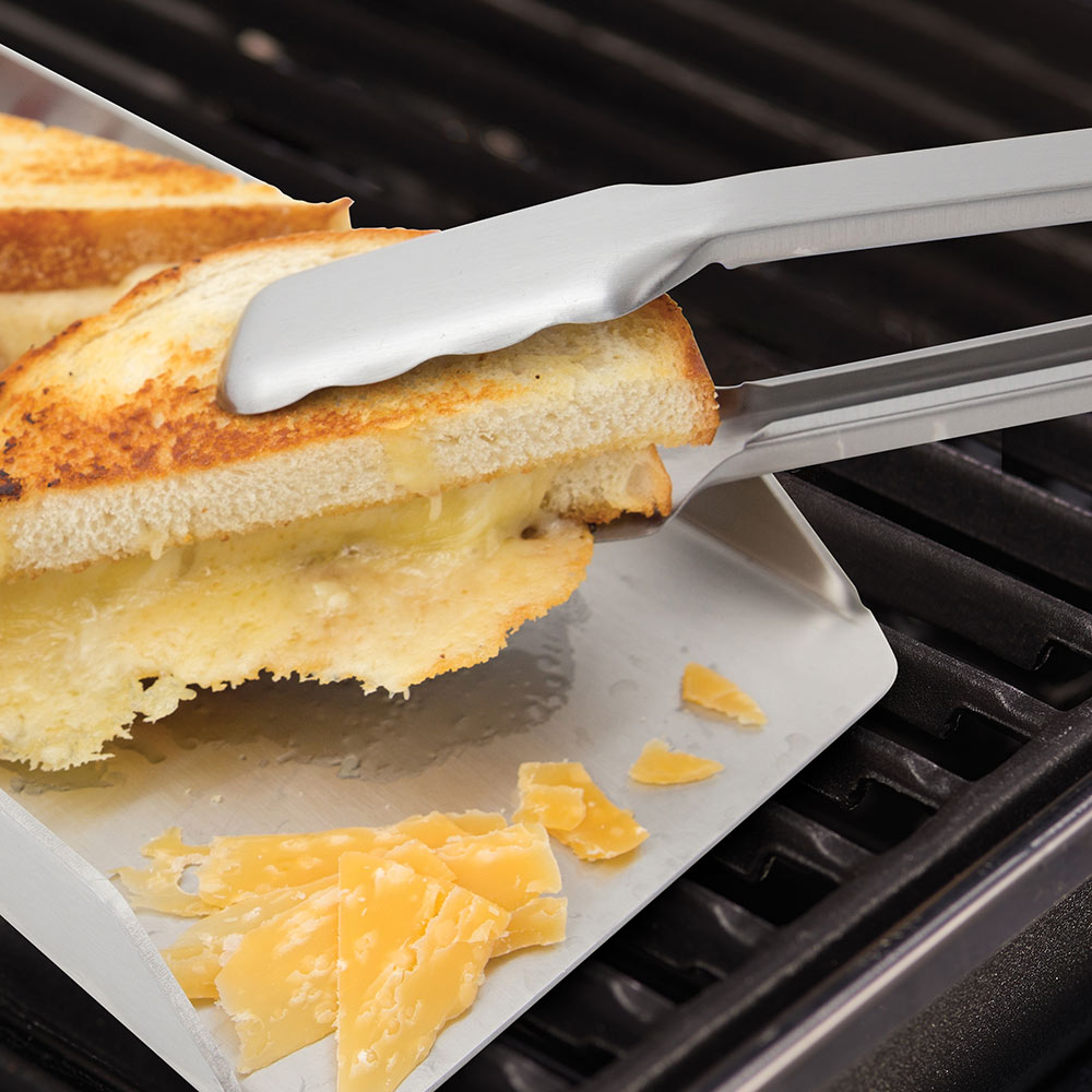 Broil King grill tongs holding toasted bread and cheese on a metal tray.
