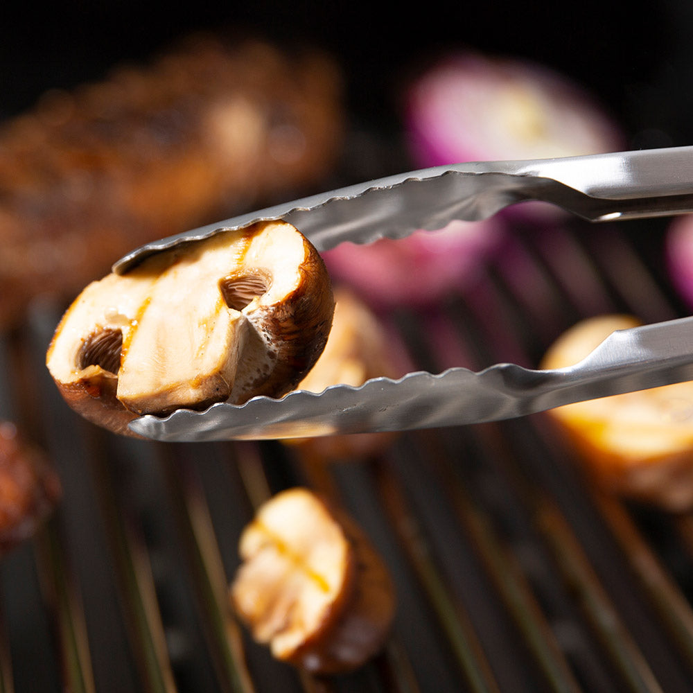 Precision tongs gripping a halved mushroom on grill grates