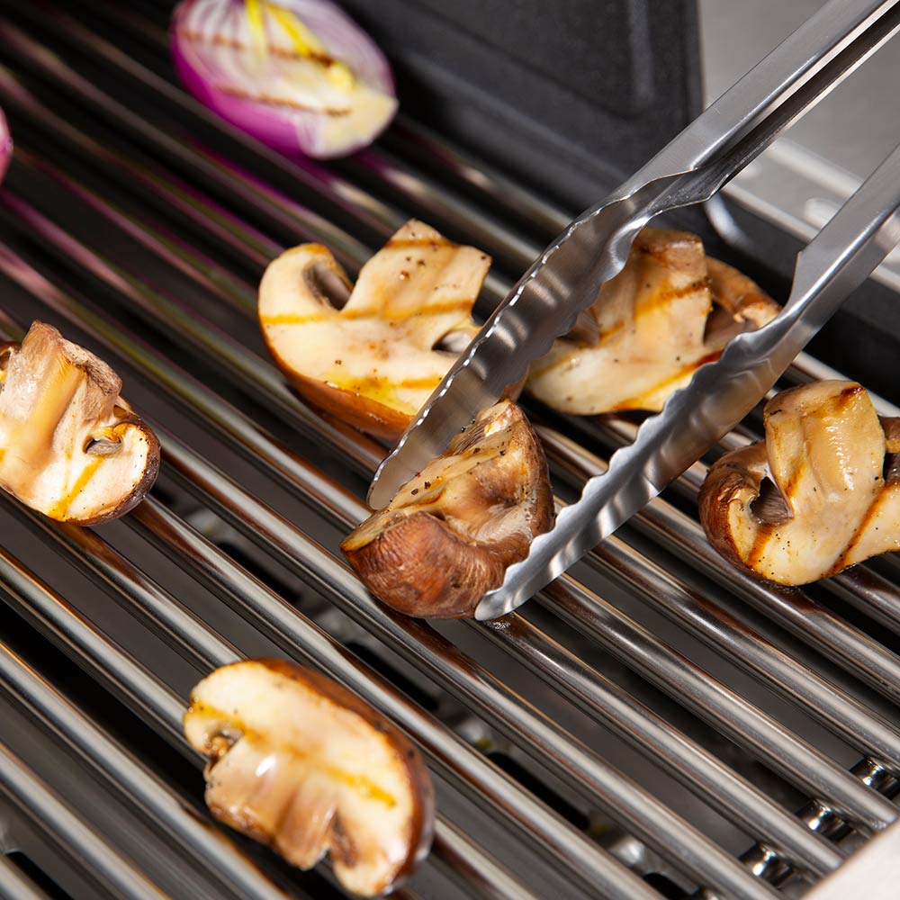 Precision tongs lifting grilled vegetable pieces on stainless grill grates