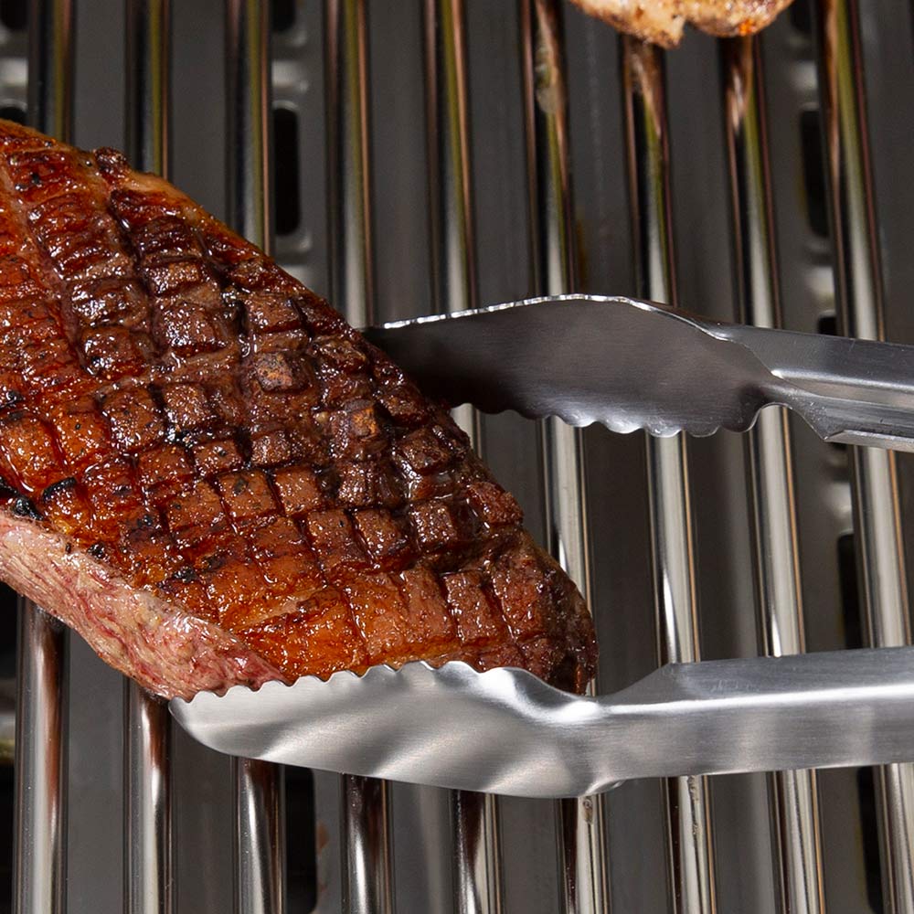 Precision tongs holding a grilled steak on stainless grill grates