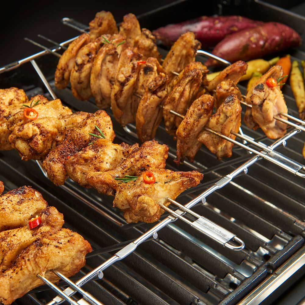 Stainless steel multi-rack skewer kit with skewers on grill grate holding seasoned chicken