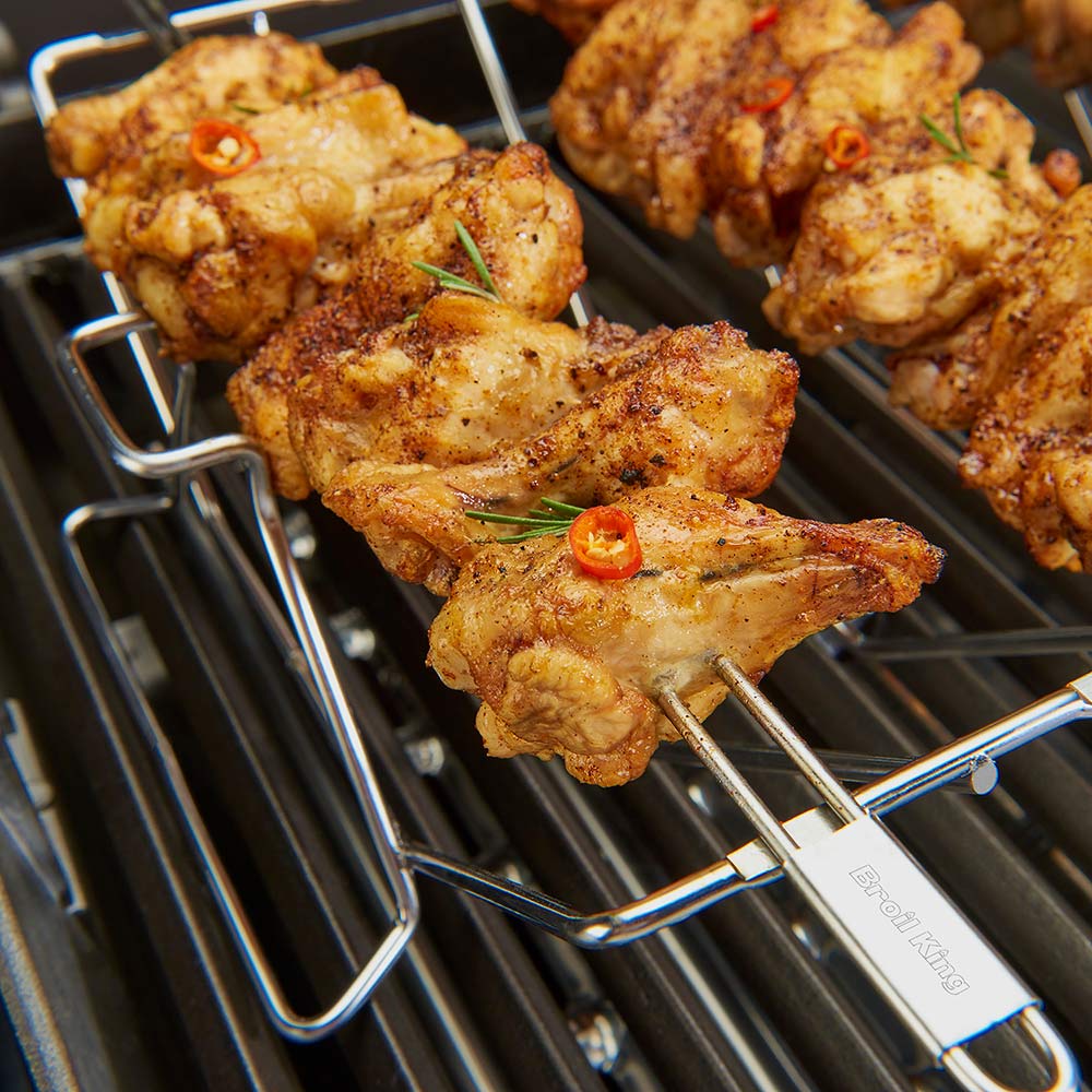 Stainless steel skewers on multi-rack holder grilling chicken on a grate