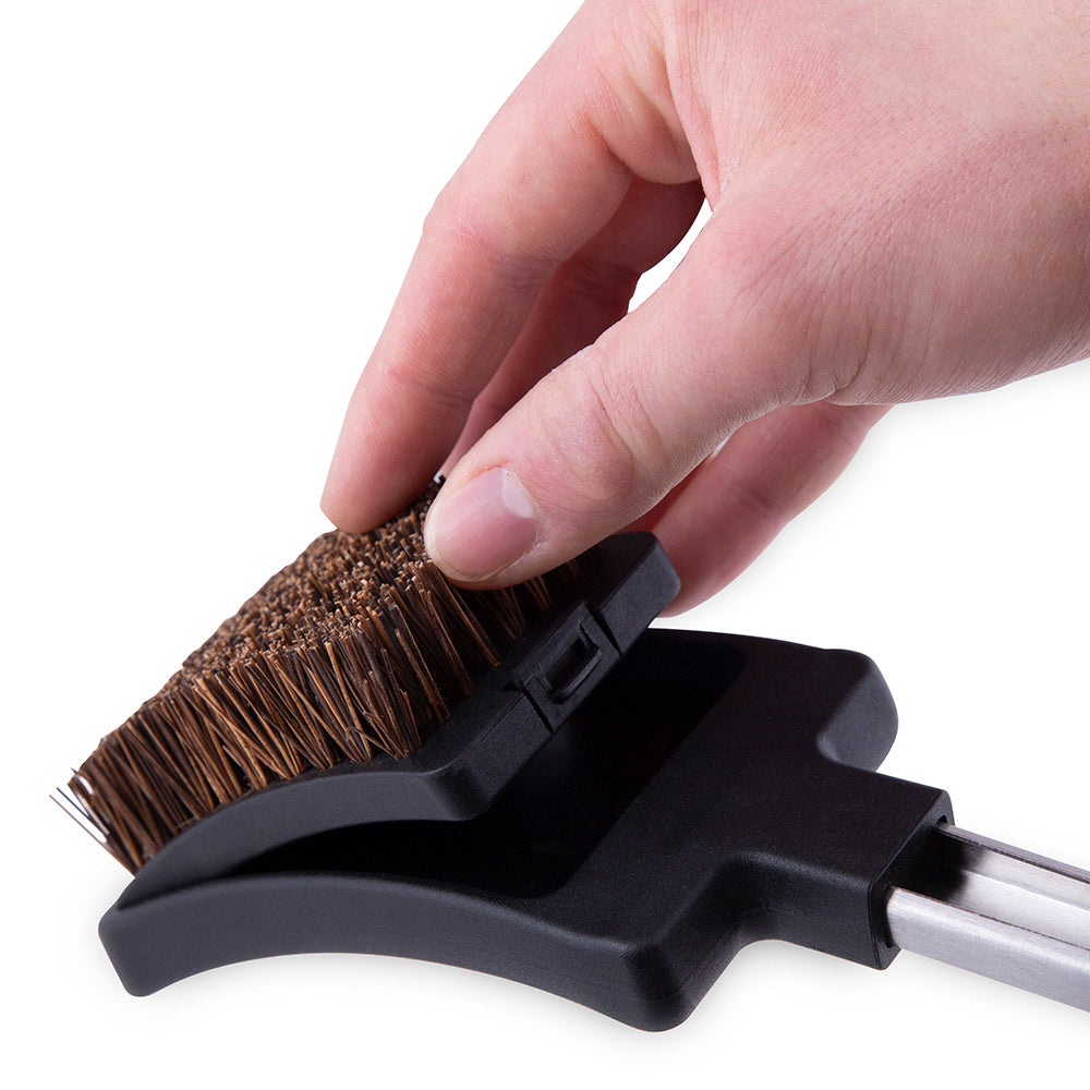 Grill brush head with black holder and brown bristles on metal rod, held by hand