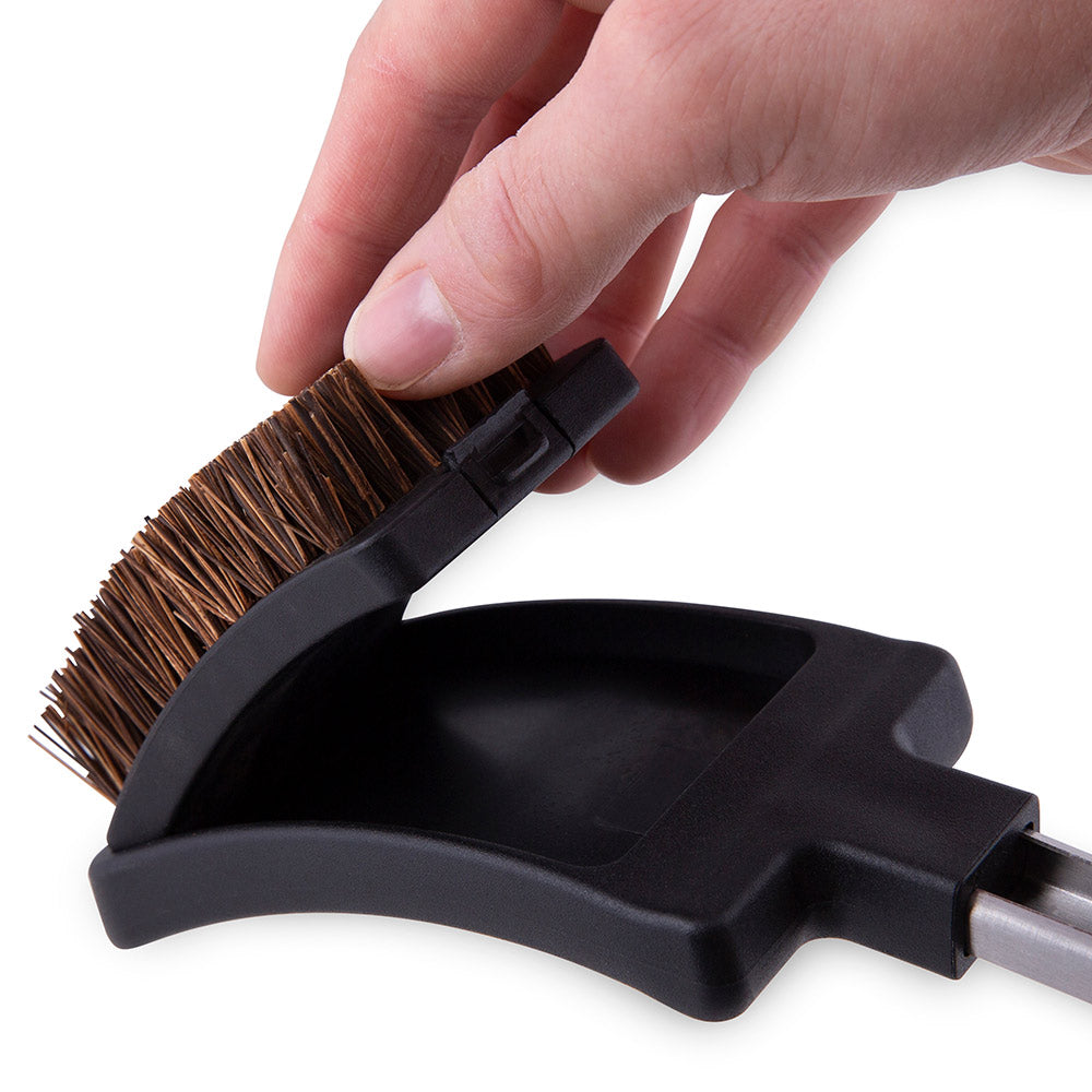 Grill brush head with black holder and brown bristles on metal rod, fingers gripping