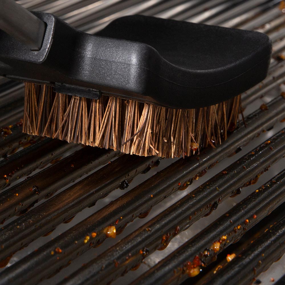 Grill brush head cleaning black grates with brown bristles attached to black handle
