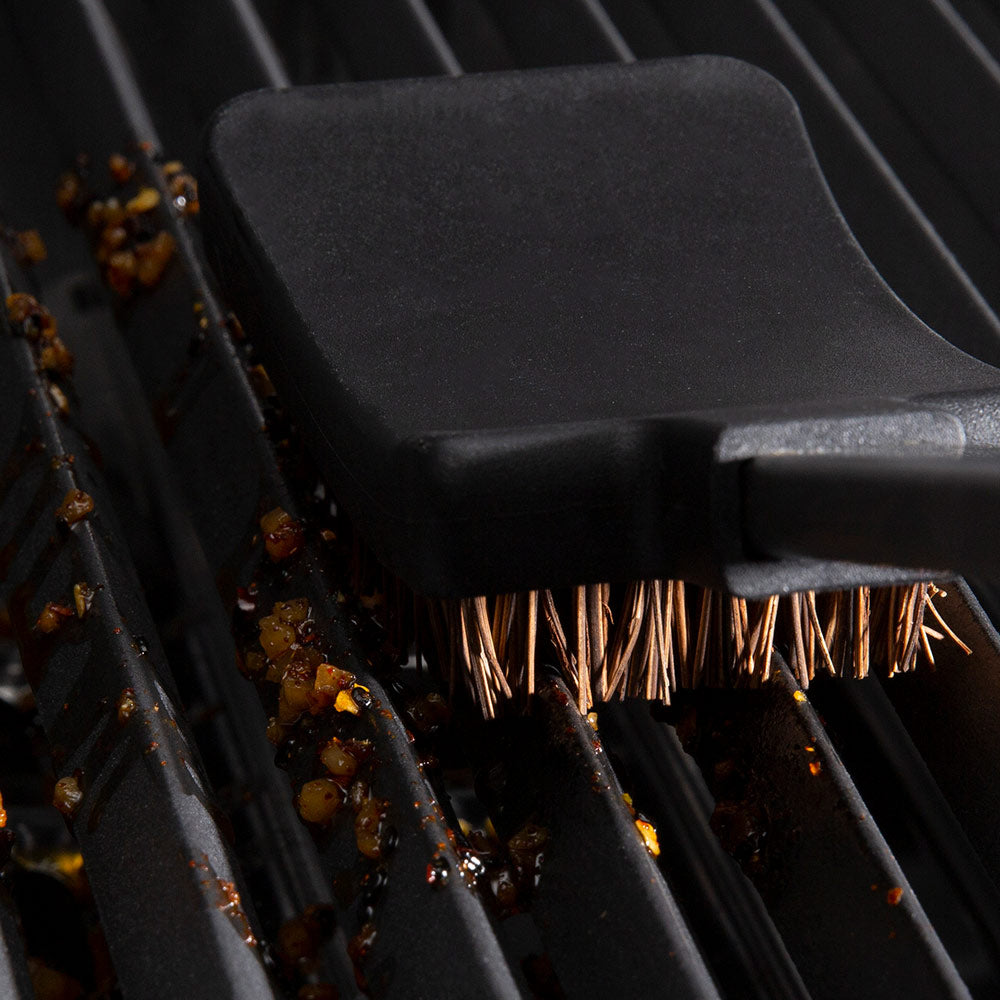 Close-up grill brush bristles with black holder scrubbing dark grates
