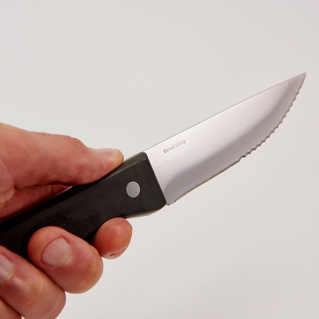 Hand holding a steak knife with black handle and stainless serrated blade