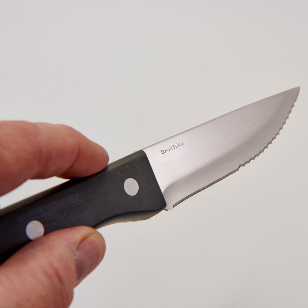 Close-up of steak knife blade with serrated edge and black handle with round rivet