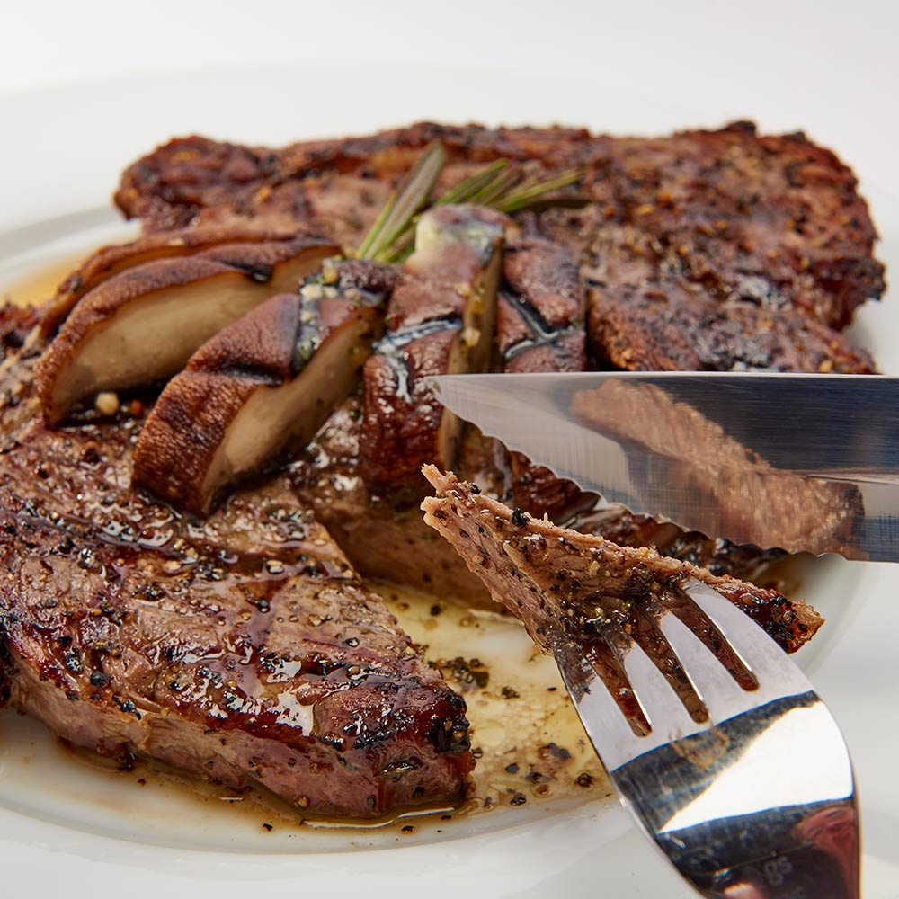 Steak knife and fork cutting cooked steak on a white plate