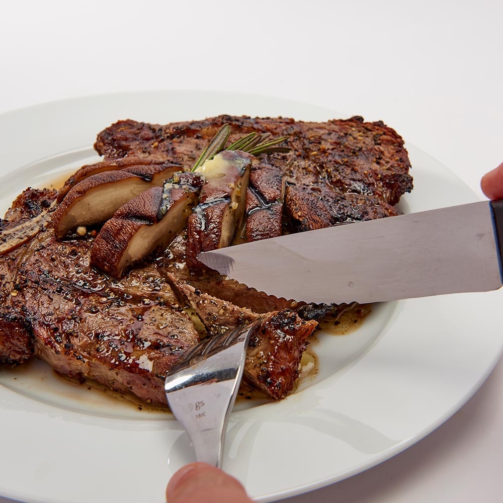 Steak knife slicing cooked steak on a white plate, black handle visible