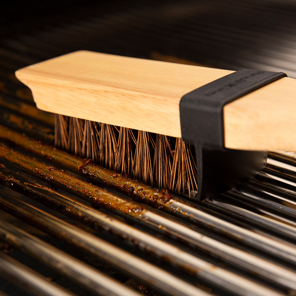Wood grill brush head with stiff bristles and dark plastic end on metal grates