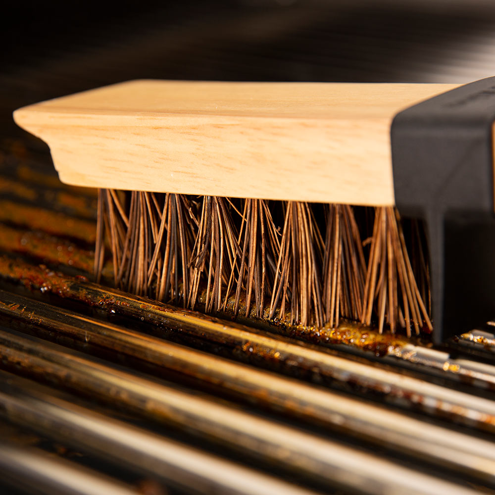 Stiff bristle grill brush head scraping grease from metal grates
