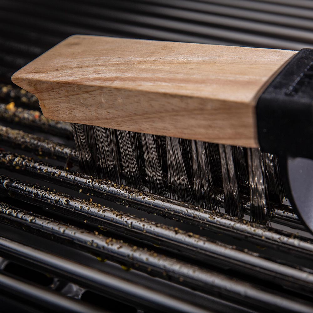 Wood-handled grill brush with dark bristles on black grill grates