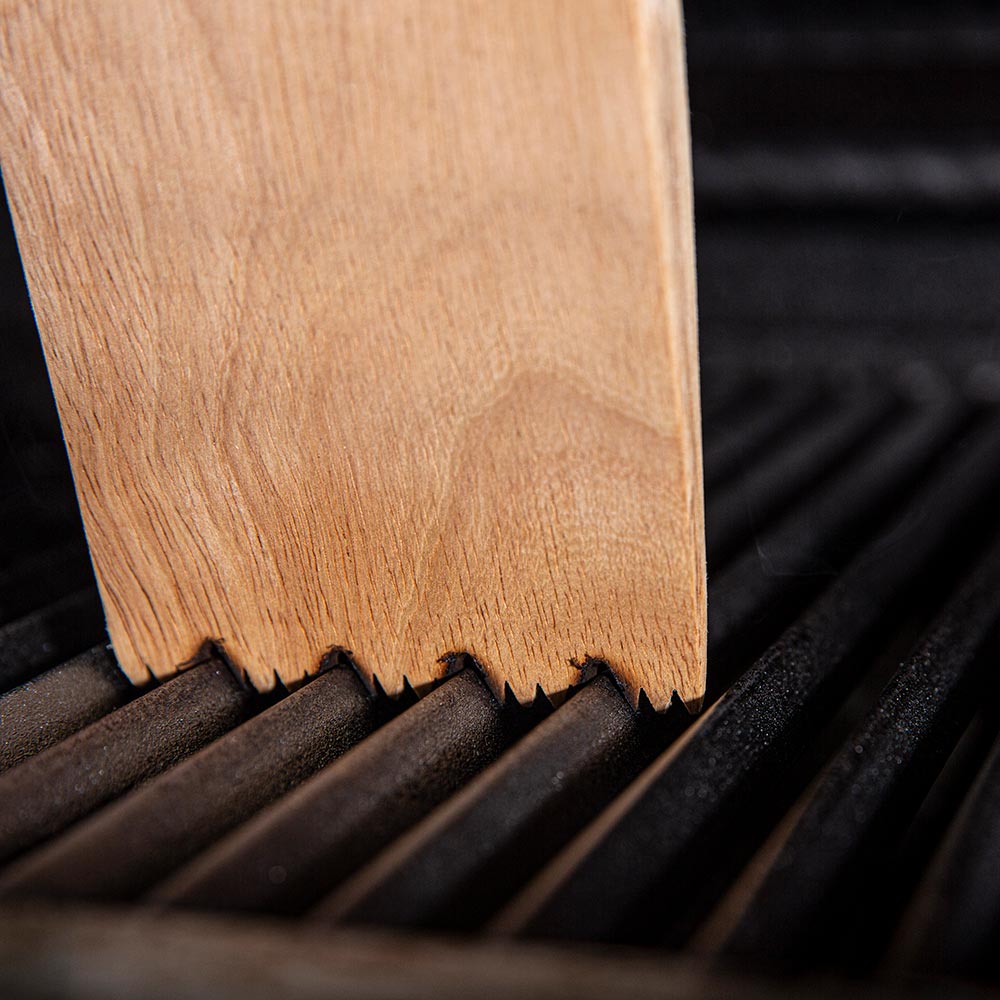 Wood grill scraper edge with jagged bristles on grill grates
