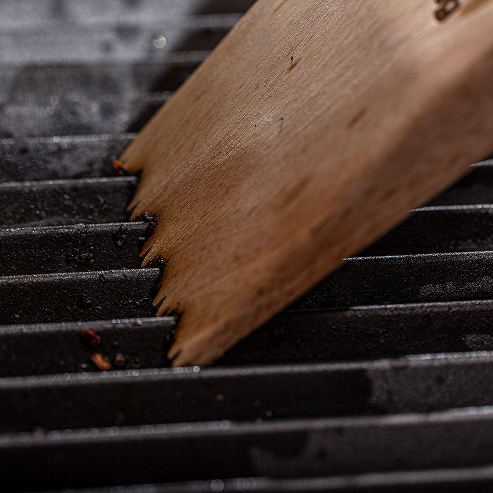 Wood grill scraper with serrated bristle edge scraping black grill grates