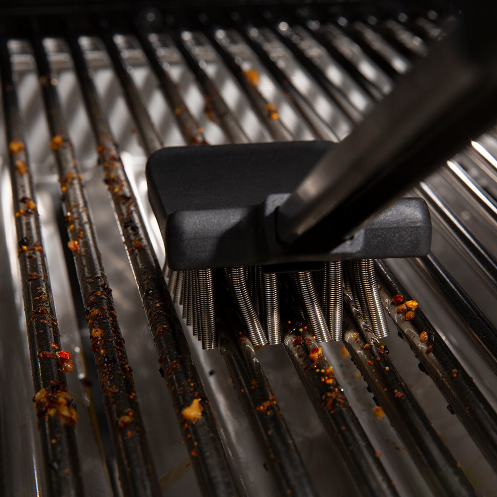 Grill brush bristles scrubbing black grates between metal rails