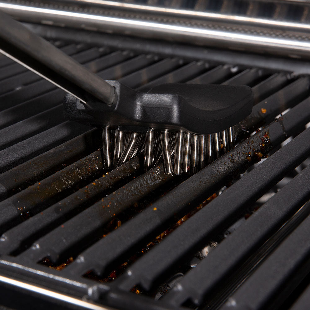 Coil spring bristles on a grill brush cleaning a grate surface with charred spots