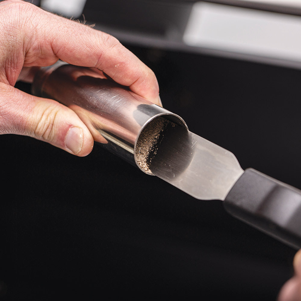 Hand using metal scraper blade to remove burnt residue from grill