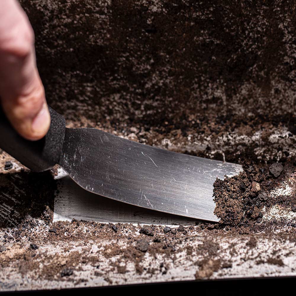 Scraper blade removing ash and grease from a grill grate