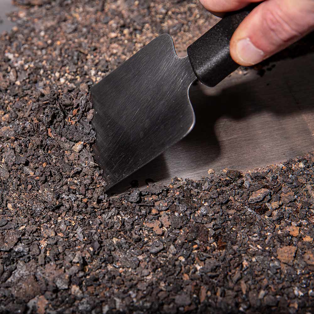 Black scraper with curved edge clearing ash from a grill grate