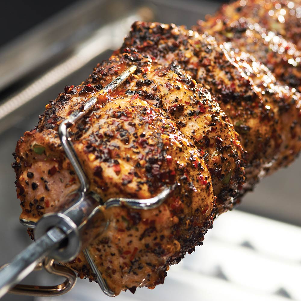 Seasoned rotisserie roast on spit with metal holding brackets