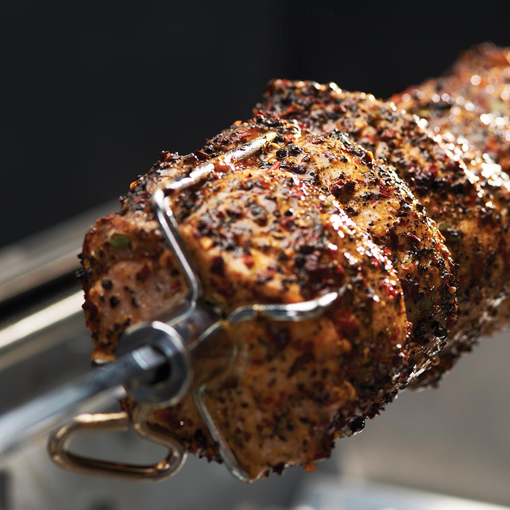 Close-up of seasoned rotisserie roast on spit with holding fork