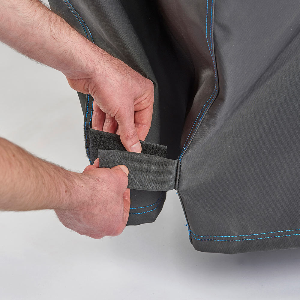 Hand fastening a strap on a black grill cover, blue-edge stitching and panels