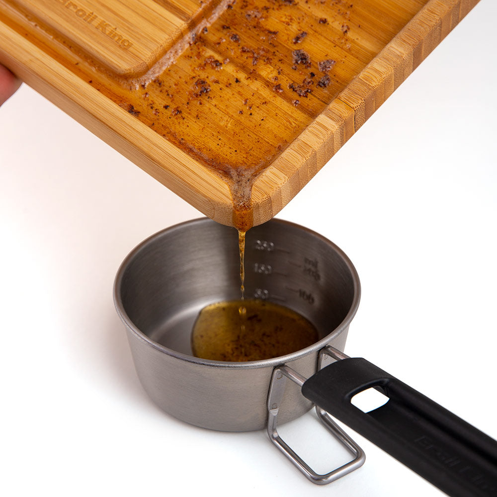 Bamboo cutting board pouring sauce into a small metal cup with handle