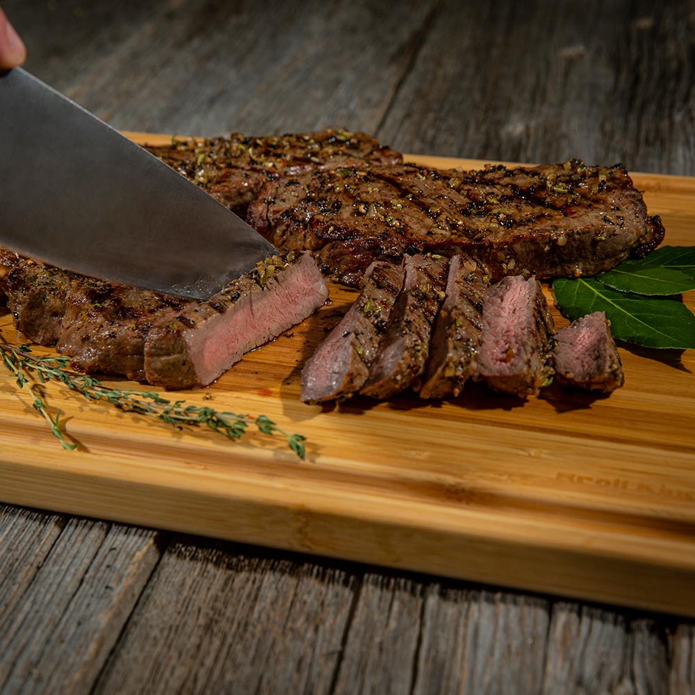 Bamboo cutting board with sliced grilled steak, herbs, and pepper-speckled seasoning
