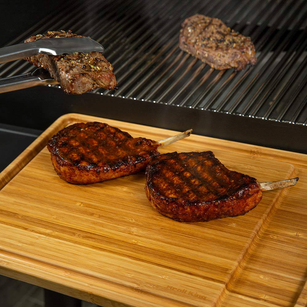 Bamboo cutting board with grilled patties and two tongs on top