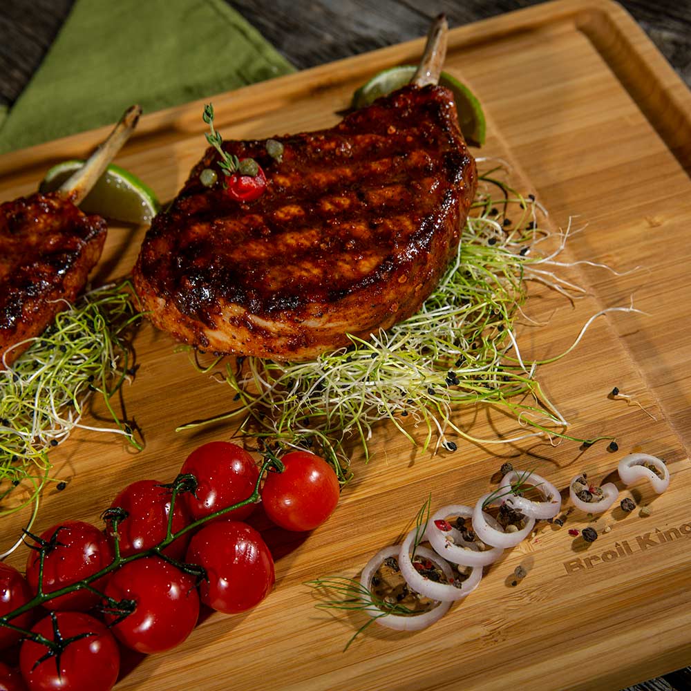 Bamboo serving board with a grilled steak, microgreens, cherry tomatoes, and herbs